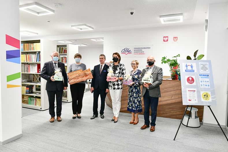 Goście wydarzenia stoją w rzędzie na tle ściany z oznakowaniem biblioteki