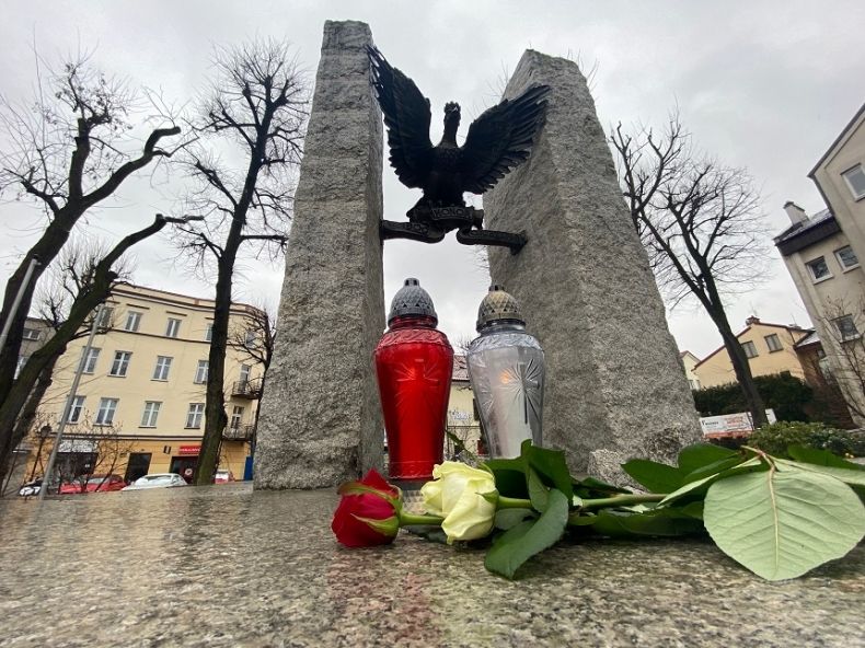 Dwa znicze i kwiaty położone na płycie pomnika. Na pomniku orzeł z rozpostartymi skrzydłami. 