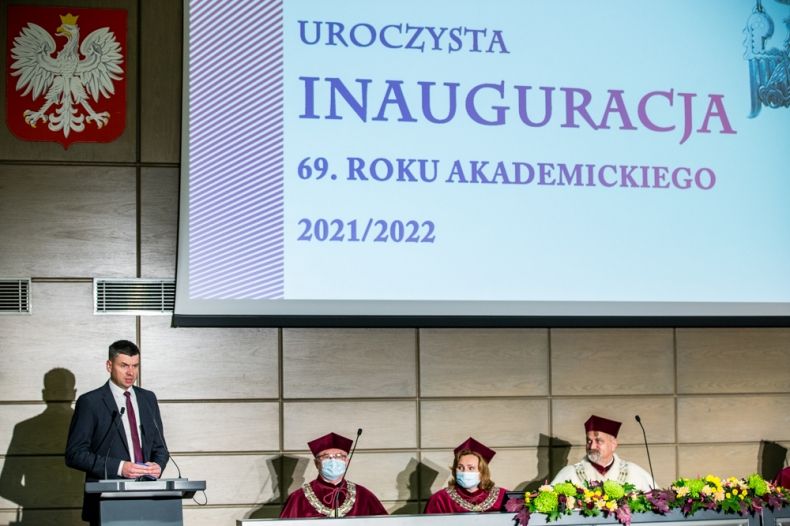 Wicemarszałek Łukasz Smółka przemawia z mównicy. Na ścianie godło Polski i napis o treści Uroczysta Inauguracja 69. roku akademickiego 2021/2022.