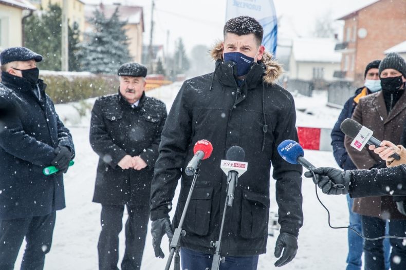 Wicemarszałek Łukasz Smółka mówi do mikrofonu podczas spotkania z mediami, w tle grupa osób