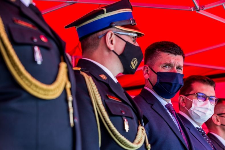 Wicemarszałek Łukasz Smółka podczas obchodów Dnia Strażaka stoi w towarzystwie oficerów straży pożarnej.