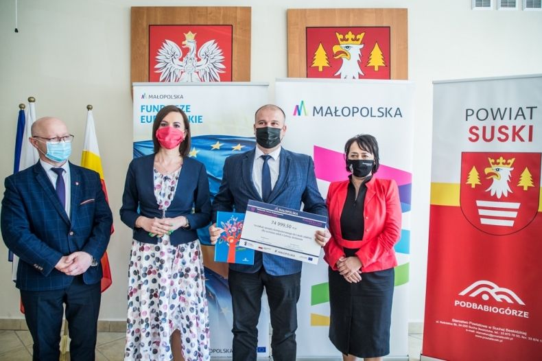 Marta Malec-Lech z zarządu województwa i radna Danuta Kawa przekazują promesy beneficjentom. W tle widoczny napis Małopolska i Fundusze Europejskie.