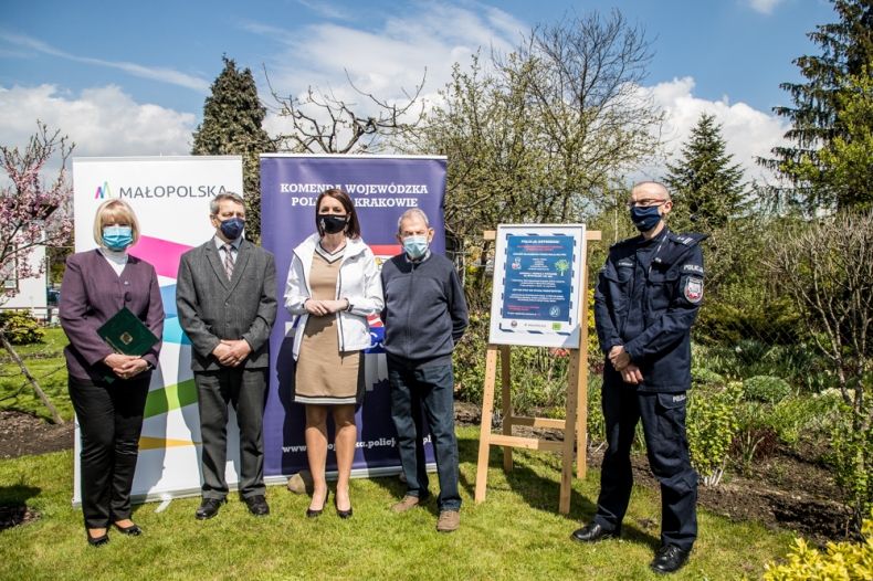 Marta Malec-Lech z zarządu województwa prezentuje plakat akcji, razem z uczestnikami wydarzenia. W tle banery z napisem Małopolska i Komenda Wojewódzka Policji w Krakowie.