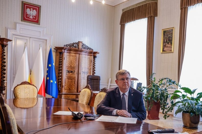 Marszałek Witold Kozłowski siedzi przy stole w gabinecie. W tle godło Polski i flagi Małopolski, Polski i Unii Europejskiej.