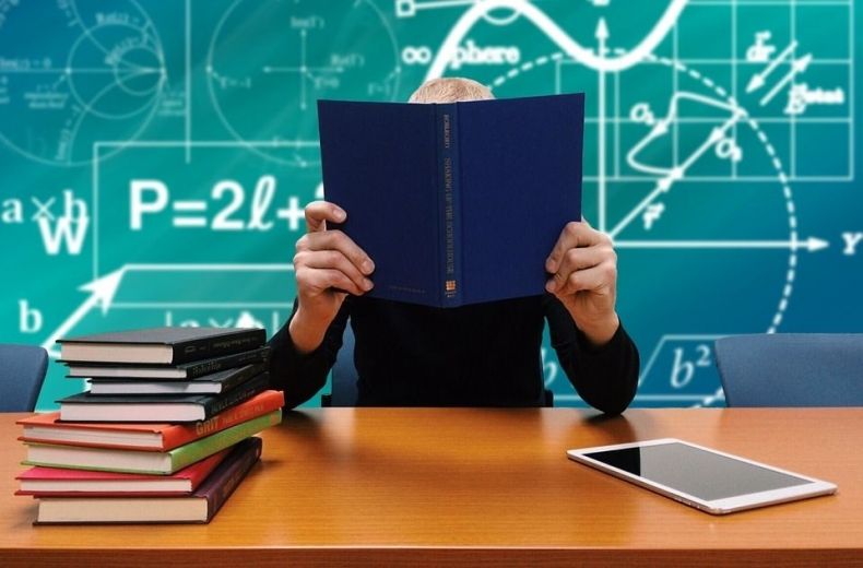 Uczeń siedzący przy biurku, stos książek leżących na biurku