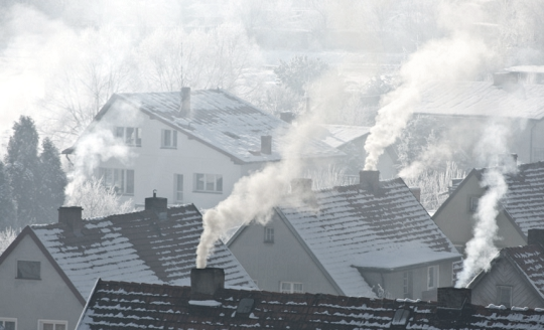 Na zdjęciu widoczne dachy domów z kominami, z których wylatuje dym.