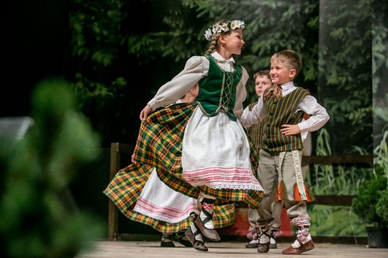 Dziewczynka i chłopczyk w strojach ludowych tańczą na scenie