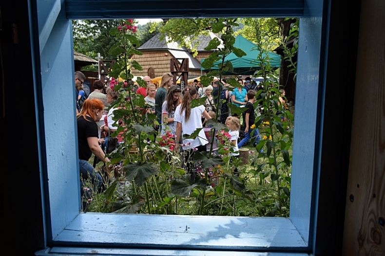 Święto Maziarzy Łosiańskich, fotografia z wnętrza chyży zrobiona przez okno na podwórko na którym jest dużo ludzi