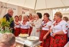 Kobiety w czerwonych strojach ludowych stoją wewnątrz białego namiotu, w śród nich stoi radna województwa Jadwiga Wójtowicz i radny Stanisław Pasoń. 