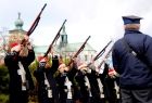 Żołnierze z karabinami mierzącymi w niebo. Z tyłu widoczny kościół.