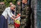 Iwona Gibas z zarządu województwa poprawia szarfę na wieńcu. Obok stoją żołnierze.