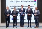 Marszałek Witold Kozłowski i wicemarszałkowie Łukasz Smółka i Józef Gawron stoją na scenie z przedstawicielem Gminy Lipnica Wielka.