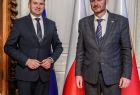 Wicemarszałek Łukasz Smółka i ambasador Jakub Dürr stoją w gabinecie. Za nimi widoczne flagi.