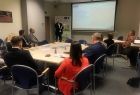 Grupa osób siedzi przy stole konferencyjnym i słucha wykładu