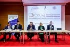 Prelegenci siedzą przy stole. Za nimi napis jest wyświetlony napis Forum wójtów, burmistrzów i prezydentów Małopolski.