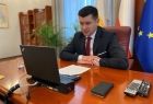 Wicemarszałek Łukasz Smółka siedzi przy biurku w gabinecie. Na pierwszym planie i w tle widoczne flagi.