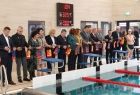 Grupa samorządowców, stoi przed basenem wypełnionym wodą, w rękach trzymają proporce w kolorach czerwonym i złotym. Przednimi widać 3 stanowiska do skoku. 