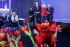 Marszałek Witold Kozłowski stoi na scenie. Na pierwszym planie widoczne czerwone kwiaty.
