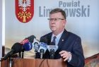 Marszałek Witold Kozłowski, stoi przy drewnianym pulpicie. Na pulpicie w kolorze brązowym ustawiono kilka mikrofonów z logami stacji radiowych i lokalnych telewizji. W tle znajduję się biła ścinaka z napisem Powiat Limanowski i godło.