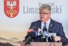 Senator Jan Hamerski, stoi przy drewnianym pulpicie, na którym wyłożono kilkanaście mikrofonów, radiowych i telewizyjnych. W tle widać białą ściankę z napisem Powiat Limanowski i herb Limanowej.