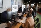 Wnętrze Tauron Areny, będące punktem nadawania nr PESEL dla uchodźców z Ukrainy. Na pierwszym Planie widać biurko, przy którym siedzi kobieta z dokumentami. Z drugiej strony widać pochyloną nad biurkiem urzędniczkę. 