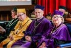 Władze Uniwersytetu Jagiellońskiego, kobieta i mężczyzna, w fioletowych szatach oraz mężczyzna w żółtych szatach siedzą podczas uroczystości.