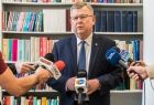 Marszałek Witold Kozłowski, stoi na tle szafy z regałami wypełnionymi Książkami. Przed nim widać iklka mikrofonów, stacji radiowych i telewizyjnych. 