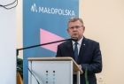 Marszałek Witold Kozłowski stoi przy mównicy, na wysokości twarzy widać czarny mikrofon. Za marszałkiem znajduję się rolap z napisem Małopolska umieszczonym na niebieskim tle. 