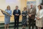Radna Marta Mordarska trzyma w ręku oprawioną w pozłacana ramę Nagrodę Polonie Minor, obok stoi marszałek Witold Kozłowski, który spogląda w stronę nagrody, obok marszałka stoi Alina Marek za nią radny Stanisław Pasoń i Iwona Mularczyk.