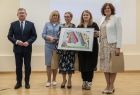 Od lewej Marszałek Województwa Witold Kozłowski, radna Marta Mordarska, dyrektor biblioteki Alina Marek i Iwona Mularczyk. Wszyscy stoją obok siebie, Alina Marek trzyma w ręku kolorowy Obrazek oprawiony czarna ramkę. 