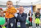 Marszałek Małopolski Witold Kozłowski unoszący do góry udekorowane dziecko z zawieszonym pamiątkowym medalem na szyi