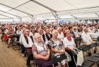 Widok na namiot, w którym zgromadzili się uczestnicy dożynek. Ludzie siedzią na krzesłach w kilkunastu rzędach. 
