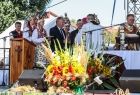 Widok na ołtarz polowy i scenę na którą wchodzą kobiety w strojach ludowych, ołtarz przyozdobiony jest bukietem wykonanym ze zboża i kwiatów. 