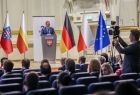 Widok na scenę filharmonii. Na której stoją Marszałek Witold Kozłowski i przedstawiciele władz samorządowych z Małopolski i Turyngii. Na scenie ustawiono flagę Polski, Małopolski, Niemczech i Unii Europejskiej. Przy mównicy stoi przemawiający mężczyzna. 