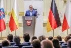 Widok na scenę filharmonii. Na której stoją Marszałek Witold Kozłowski i przedstawiciele władz samorządowych z Małopolski i Turyngii. Na scenie ustawiono flagę Polski, Małopolski, Niemczech i Unii Europejskiej. Przy mównicy stoi przemawiający mężczyzna. 