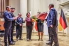 Marszałek Witold Kozłowski i przedstawiciele władz samorządowych z Małopolski i Turyngii. Kobieta stojąca na scenie trzyma kwiaty. Marszałek Witold Kozłowski wręcza drugi bukiet kwiatów. 