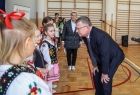 Marszałek Małopolski Witold Kozłowski wita się z dziećmi . Uczniowie maja na sobie stroje ludowe i stoją w sali gimnastycznej. 