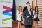 Dyrektor Szkoły podstawowej w Łabowej stoi przed mikrofonem, za nią widać troje uczniów i rolap z logiem małopolski. 