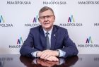marszałek siedzi za stołem na tle ścianki z logo Małopolski 