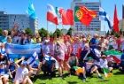 Sportowcy z różnych krajów trzymający flagi pozują do wspólnego zdjęcia na tle zieleni