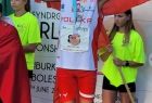 Zawodnik z Polski pozuje z biało-czerwoną flagą stojąc na podium, w tle hostessy