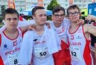 Czterech zawodników w biało-czerwonych strojach stoi na bieżni, trzymając flagę narodową