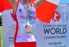 Zawodniczka w biało-czerwonym stroju stoi na podium trzymając flagę