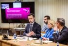 Uczestnicy posiedzenia siedzą przy stole konferencyjnym, w tle ekran z wyświetlaną prezentacją