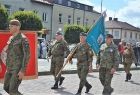 Żołnierze maszerują przez rynek ze sztandarem.