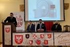 Wojewoda Łukasz Kmita mówi do zgromadzonych na sali gości. W tle widoczne zdjęcie rezonansu magnetycznego.