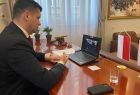 Wicemarszałek Łukasz Smółka patrzy na ekran laptopa podczas konferencji. Po prawej widoczne flagi, na ścianie wisi obraz.