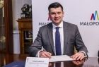 Wicemarszałek Łukasz Smółka siedzi przy stole i podpisuje umowę.
