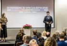 Wicemarszałek Łukasz Smółka przemawia na scenie. Obok stoi kobieta prowadząca imprezę. Za nim jest wyświetlany napis Konferencje Specjalistyczne.
