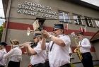 Strażacy z orkiestry grają. Z tyłu napis na budynku Ochotnicza Straż Pożarna w Nowej Górze.
